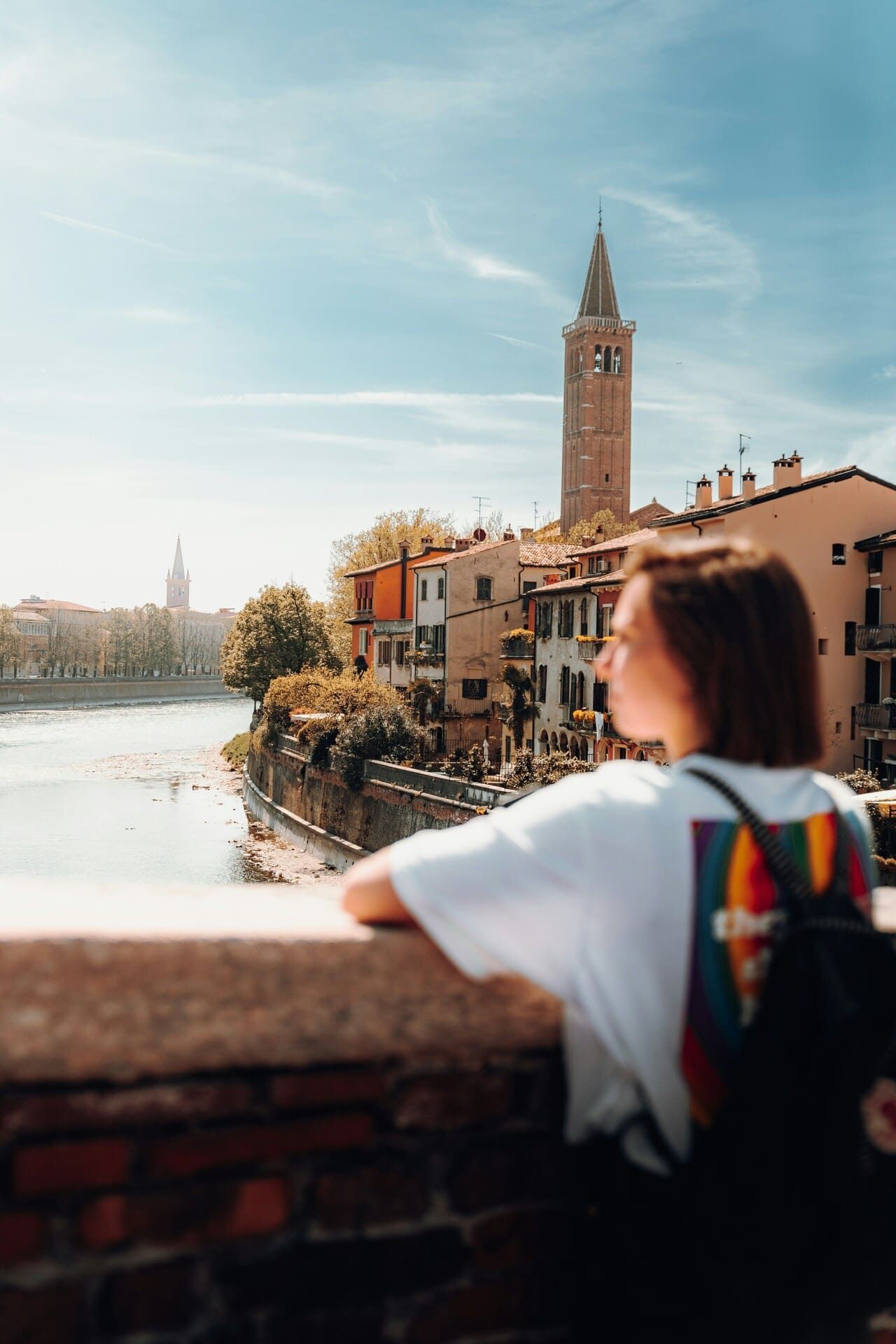 Giovane ragazza in primo piano si affaccia a un ponte e si scorge Verona sullo sfondo